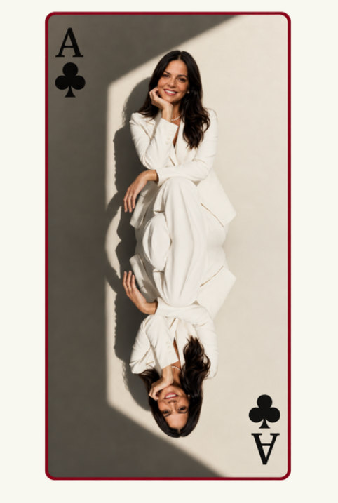 Gabriela Agapito retratada como a carta ás de paus, de terno branco e sorrindo