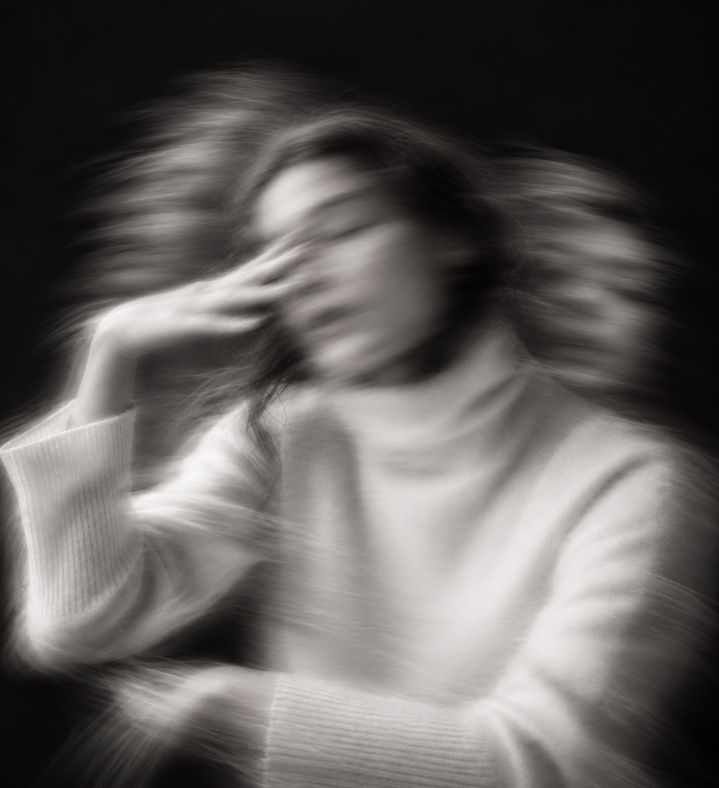 Mulher de suéter claro com a mão no rosto, em fotografia preto e branco com efeito de movimento